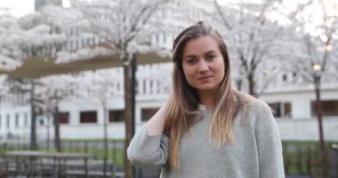 Güzel sarışın kameraya poz verir ve gülümseyerek saçını düzeltir.