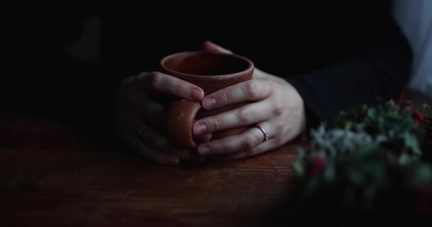 Close-up mãos abraçar uma cerâmica marrom segurando em uma mesa de madeira — Vídeo de Stock
