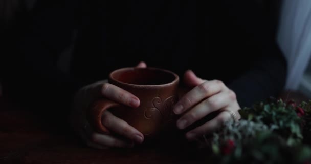 Las manos de cerca abrazan una taza de cerámica marrón en una mesa de madera — Vídeo de stock