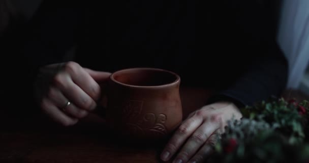 Крупним планом руки обіймають і крутять коричневий керамічний кухоль на дерев'яному столі — стокове відео