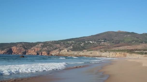 岩の多い海岸を背景に、海の砂漠の海岸に泡立つ波 — ストック動画