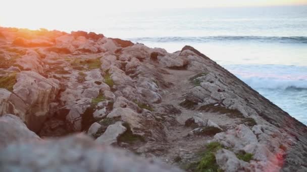 Солнце размышляет над камнем на берегу океана на фоне пенных волн — стоковое видео