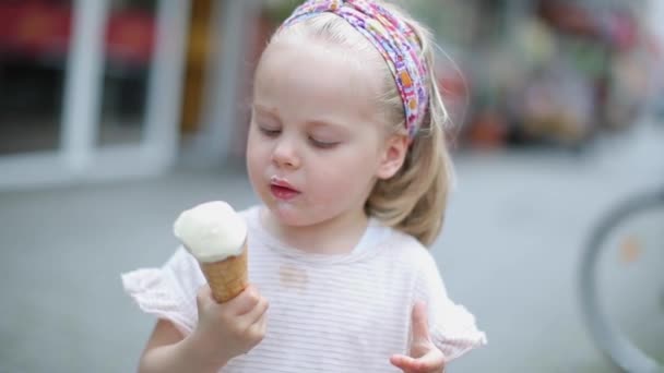 In the city on the street little beautiful girl blonde eats ice cream — Stock Video