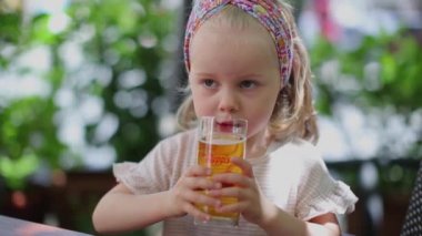Sarışın, küçük güzel bir kız uzun cam bardaktan meyve suyu içiyor.