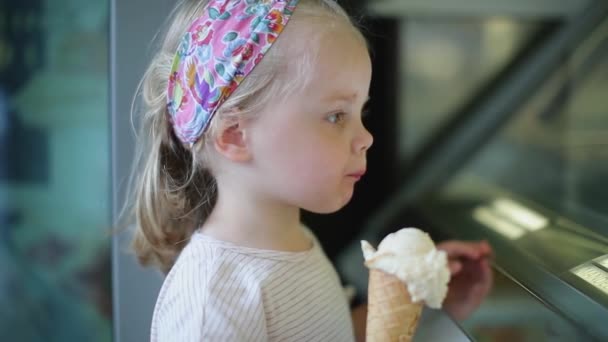 Little blonde stands near the window and eats ice cream — Stock Video