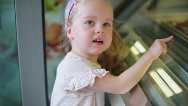 Uma menina com cabelo branco escolhe um slot de compras na janela da loja — Vídeo de Stock