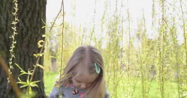 Hermosa rubiecita se para en el parque de primavera entre las ramas verdes de árboles largos — Vídeos de Stock
