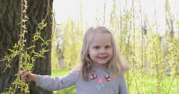 Close-up bambina bella sorride nel parco primaverile tra rami di alberi verdi — Video Stock