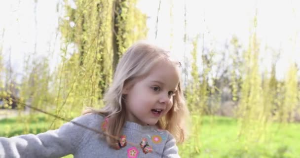 Dans le parc du printemps, une belle petite fille blonde court parmi les branches vertes 