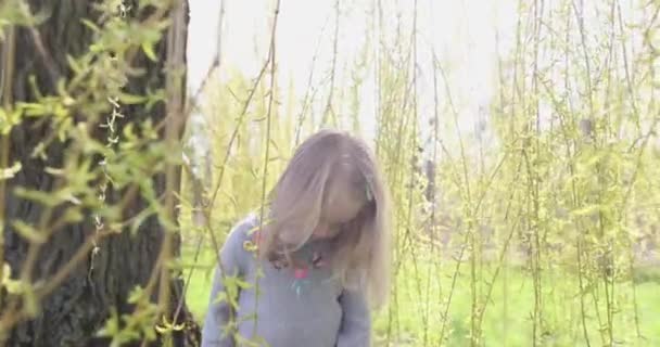 Egy kislány a tavaszi parkban zöld, hosszú faágakkal játszik. — Stock videók