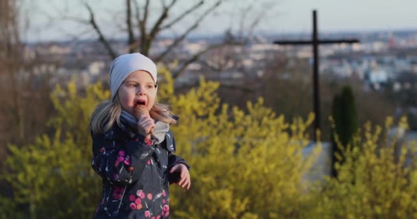 En vacker liten flicka med vitt hår äter glass i parken — Stockvideo