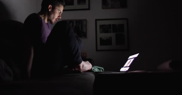L'homme dans une pièce sombre s'assoit sur le canapé et regarde l'écran de l'ordinateur portable 