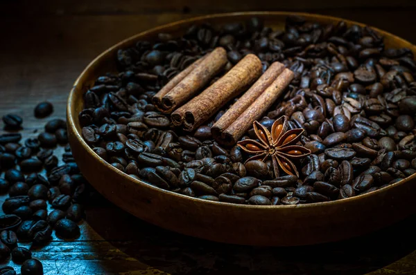 Coffee beans and cinnamon sticks in wooden bowl on wooden table.