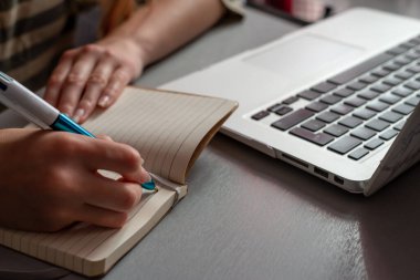 Evde çalışan genç bir kadın, not defterine yazan öğrenci kız & bilgisayara bakıyor, online alışveriş yapıyor, evden çalışıyor veya okuyor, serbest çalışıyor, çevrimiçi öğreniyor, uzaktan eğitim kavramı