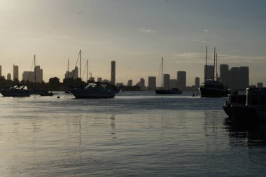 Körfezde günbatımı suyu ön planda tekneler ve arka planda gökdelenler.