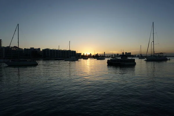 手前にボート 奥に高層ビルがある湾の夕日の水 — ストック写真