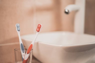 Cepillos de diente en un vaso de cristal dentro en el lavabo