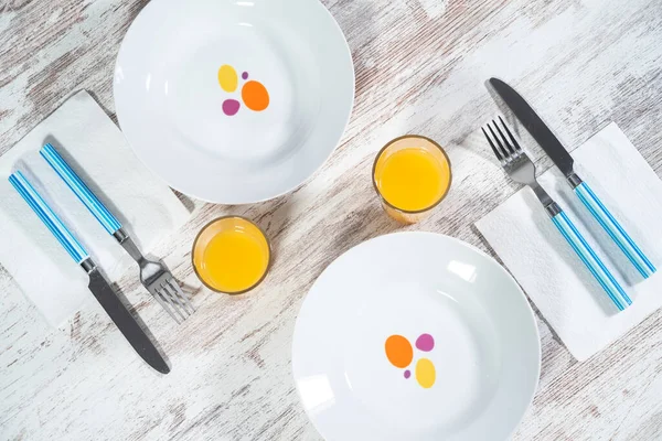 Mesa de madera prepare ada para el desayuno con dos platos, cubiertos y dos vasos de zumo de naranja
