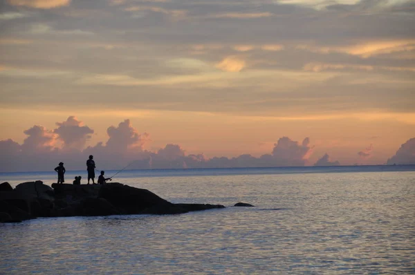 La gente pesca sugli scogli vicino al mare al tramonto — Foto Stock