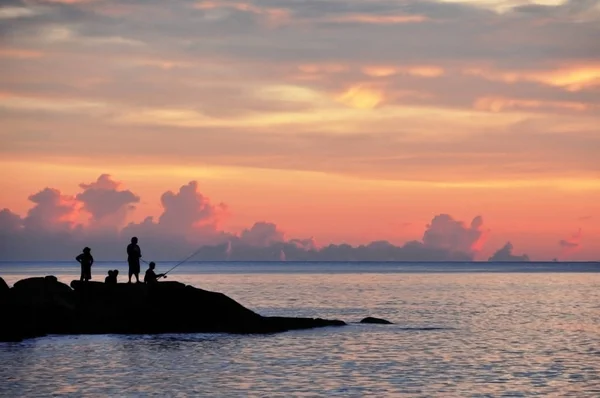 La gente pesca sugli scogli vicino al mare al tramonto — Foto Stock