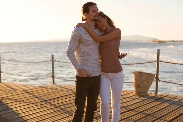 Una joven pareja romántica está de pie en el puente de madera cerca del mar y abrazándose — Foto de Stock