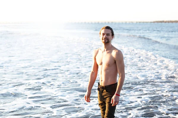 Un beau jeune homme est debout dans la mer, le soleil brille — Photo