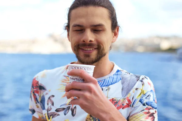 Un jeune homme beau prenant un café chaud à l'extérieur près de la mer profitant de ce moment — Photo
