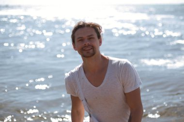 yakışıklı, seksi ve genç bir adam mavi denize yakın duruyor ve sana bakarken, güneş parlıyor