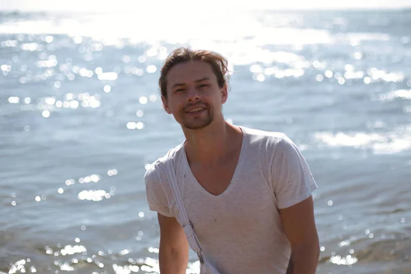 Un beau jeune homme sexy se tient près de la mer bleue et vous regarde, le soleil brille — Photo