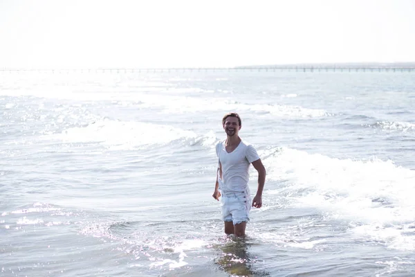 Przystojny seksowny młody człowiek stoi w błękitne morze i słońce patrzy na Ciebie, — Zdjęcie stockowe