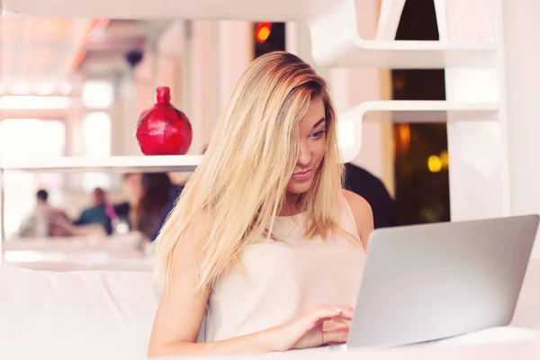 Una hermosa joven mujer de negocios rubia está trabajando en una computadora portátil en un café temprano en la mañana — Foto de Stock