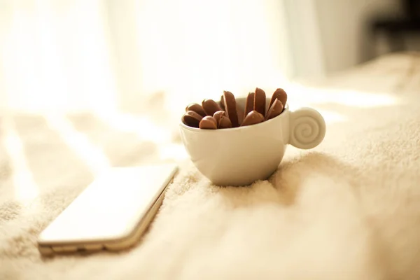 A cup of coffee or tea with chocolate biscuits  standing on the bed early in the morning with a mobile phone next to it — Stock Photo, Image