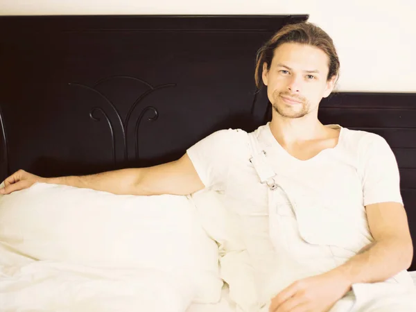 Un jeune homme beau se relaxe au lit à l'hôtel pendant les vacances par temps chaud et vous regarde — Photo