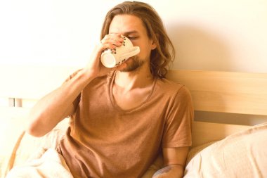 yakışıklı bir genç adam yatağında uyanmak sonra bir fincan sıcak çay içme elinde çay ile yatıyor