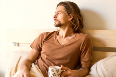 ciddi bir genç adam hakkında bir şey düşünüyorum, uyku modundan çıkarma sonra yatakta yatan elinde çay ile pencereden dışarı bakıyor