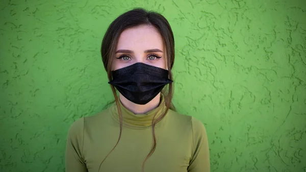 Bella ragazza sullo sfondo verde con maschera medica nera. Protetto e salvato dai problemi respiratori . — Foto Stock