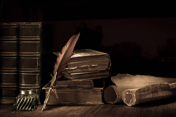Quill pen and a rolled papyrus sheet on a wooden table with old books, vintage effect