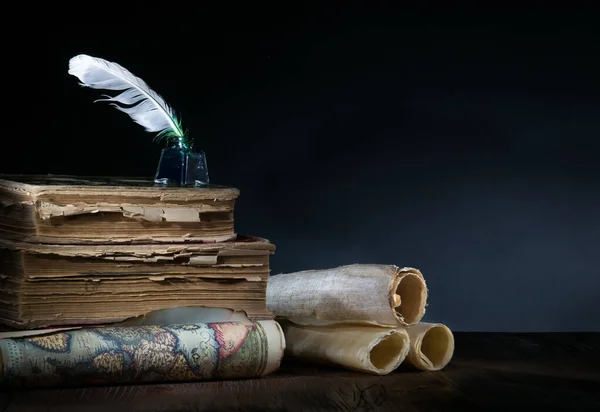 Quill pen, inkwell, old rolled up maps and papers on a dark background