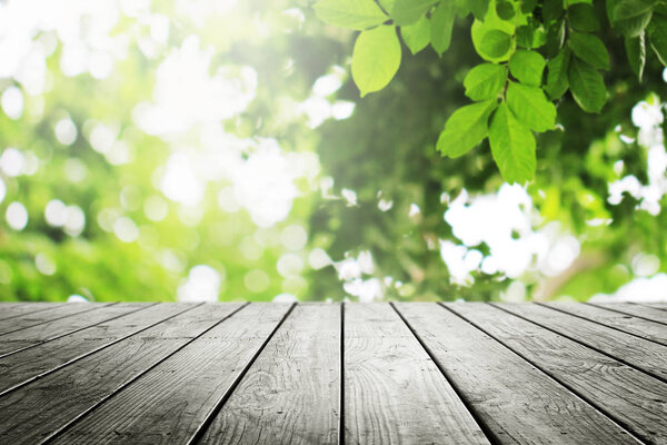 Wooden table with beautiful sunlight and blurred green leaves nature in the garden bokeh background.