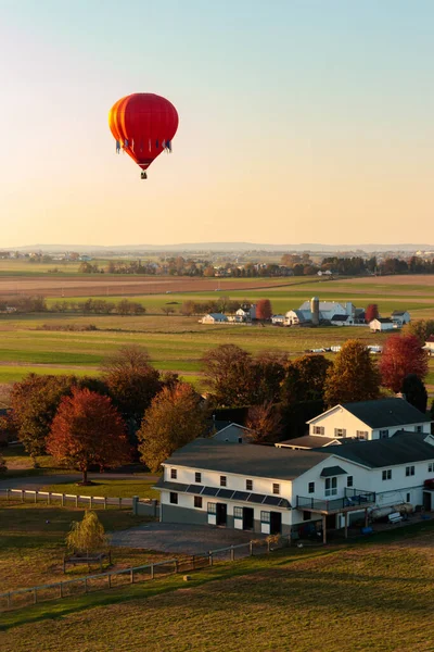 Single red hot air balloon flying above a farm during early morning.