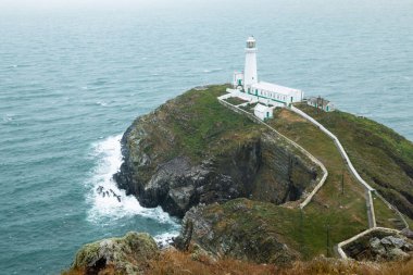 Tarihi Güney Yığını Deniz Feneri, sarp kayalıklardan 400 adım aşağıya inen küçük bir adada yer almaktadır. Güney Yığını Kayası, Holyhead Adası 'ndan 30 metre dalgalı denizle ayrılmış ve sürekli gidip geliyor.