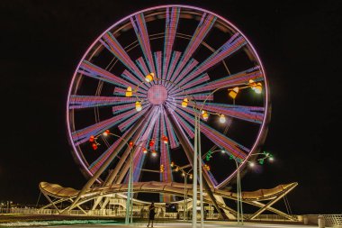 Geceleri renkli bir dönme dolap. Ön manzara. Bakü 'de büyük bir atlıkarınca. Gece eğlencesi. Dönme dolap karanlık bir gökyüzü arka planına karşı. Dönme dolap ve lunapark treni hareket halinde. Uzun pozlama ışığı