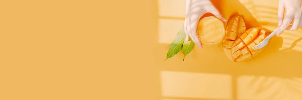 İnternet afişi ve düz yaz meyveleri güzellik kadınının elinden tut mango suyu ve mango dilimi için çatal kullan tropikal yaprağın gölgesi ve sarı arka planla birlikte.
