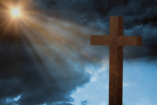 Композитное изображение деревянного креста на фоне голубого неба над травой
