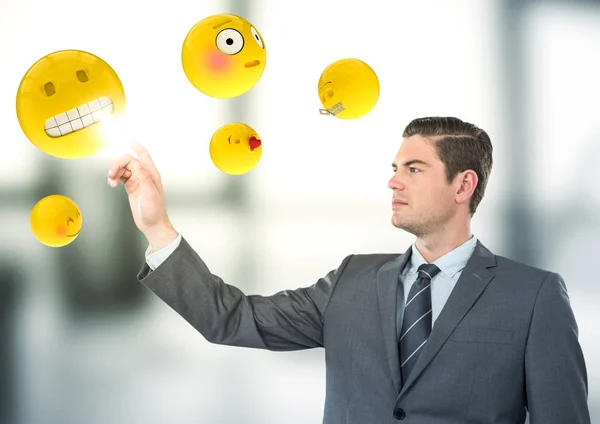 Affärsman som pekar på emojis mot suddiga grå office — Stockfoto