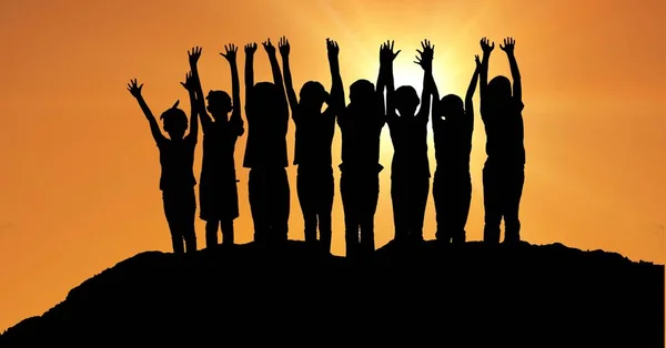 Silueta děti s rukama nad hlavou na kopci proti oranžové obloze — Stock fotografie