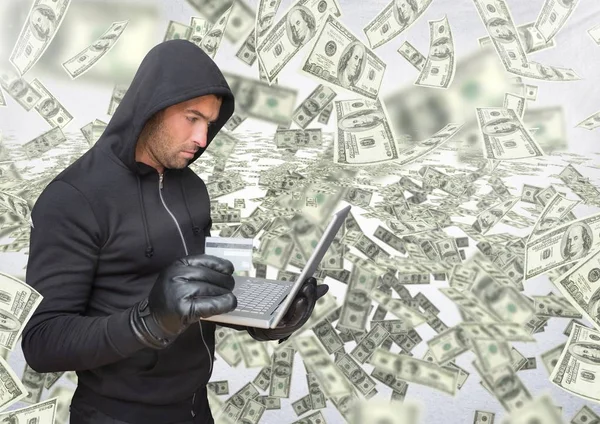 Kriminella i huven på laptop framför massor av pengar — Stockfoto
