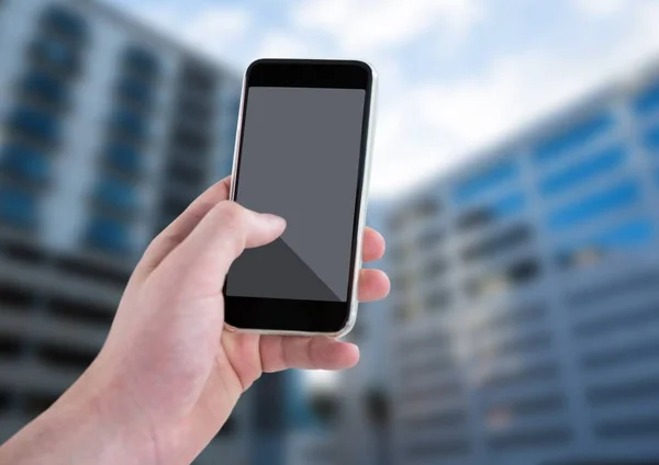 Hand met telefoon tegen wazig gebouwen — Stockfoto
