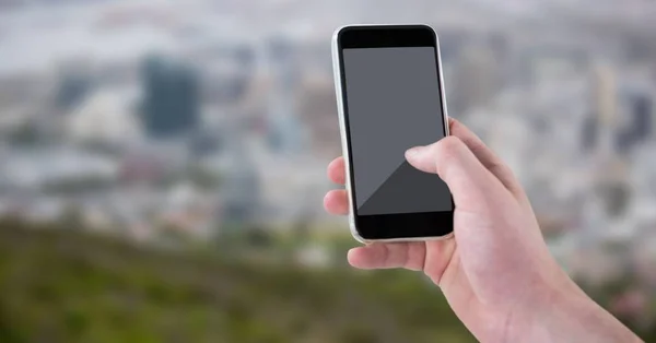 Hand med telefonen mot suddiga skyline — Stockfoto