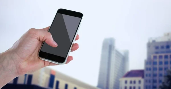 Mão com telefone contra edifícios embaçados — Fotografia de Stock